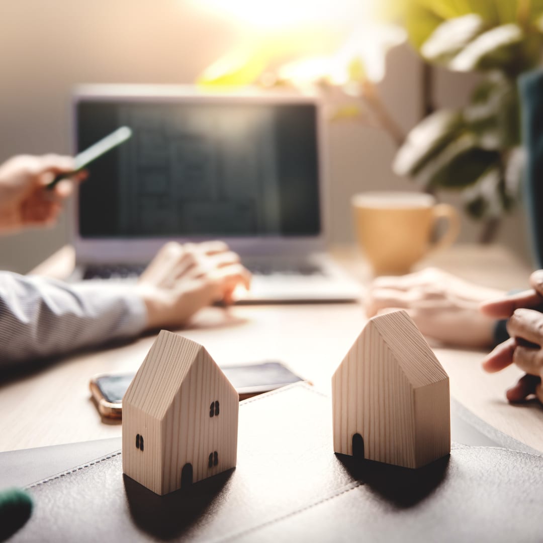 Two model houses and a laptop on a desk during a home-selling strategy consultation
